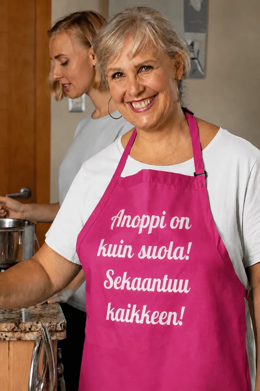 Vaaleanpunainen hauska esiliina, jossa valkoinen teksti Anoppi on kuin suola! Sekaantuu kaikkeen!