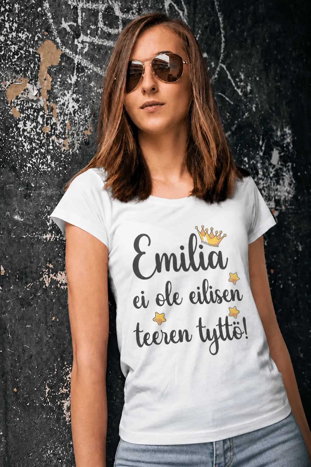 Nainen valkoisessa nimikoidussa T-paidassa, kruunu ja teksti ”Emilia ei ole eilisen teeren tyttö!”