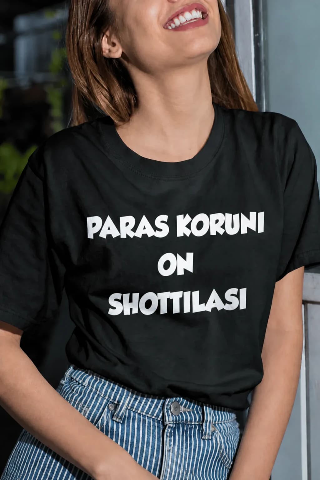 Nauravainen nainen mustassa T-paidassa, jossa valkoinen teksti Paras koruni on shottilasi