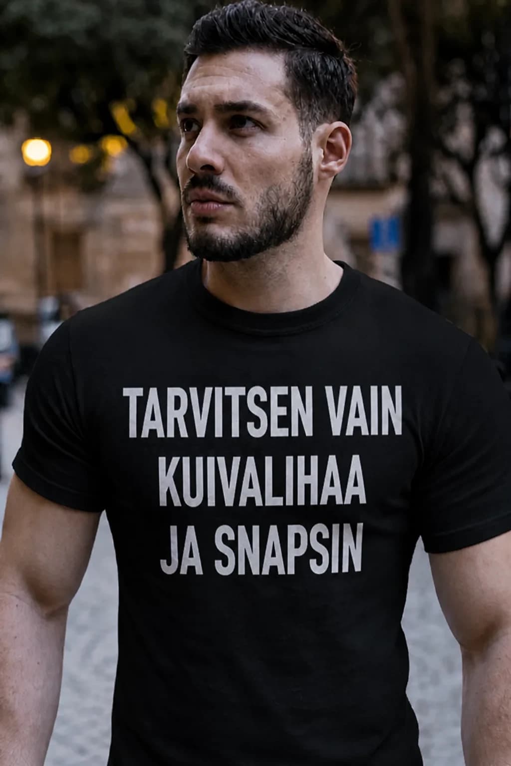 Mies mustassa T-paidassa, jossa teksti Tarvitsen vain kuivalihaa ja snapsin – hauska T-paita