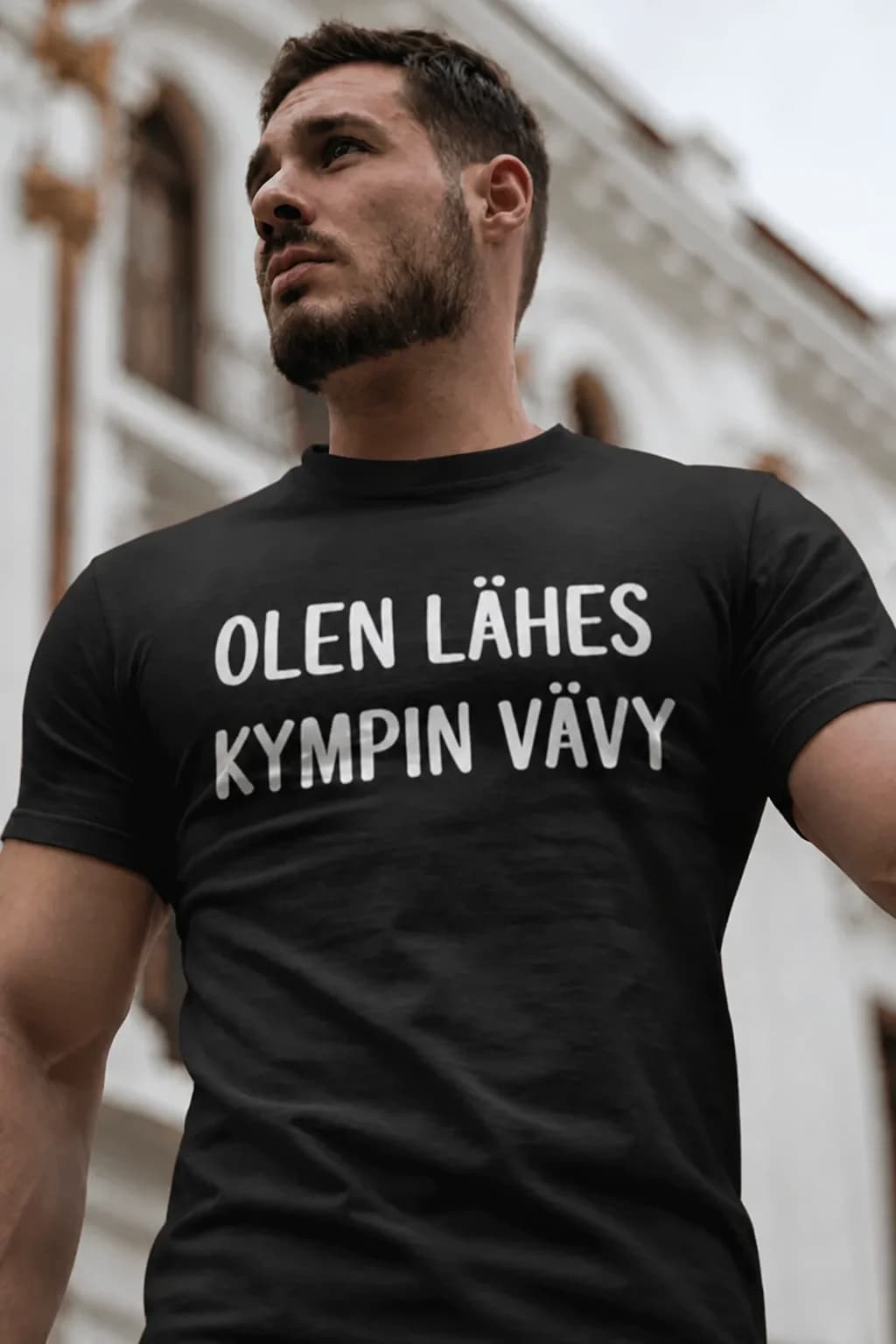 Mies mustassa T-paidassa vävylle, jossa valkoinen teksti olen lähes kympin vävy, lahja anopilta