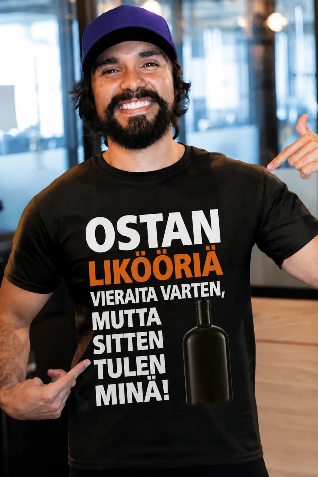 Parrakas mies mustassa hauskassa T-paidassa, jossa pullo ja teksti ostan vieraita varten, mutta sitten tulen minä