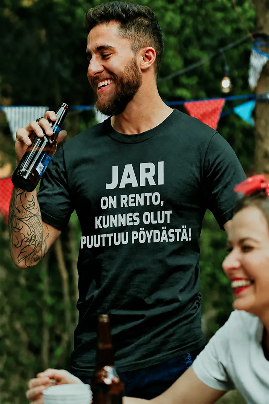 Mies olutpullon kanssa mustassa T-paidassa, jossa teksti JARI ON RENTO, KUNNES OLUT PUUTTUU PÖYDÄSTÄ!