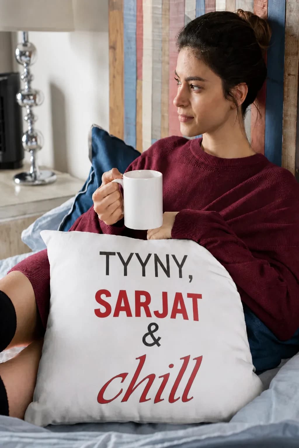 Valkoinen koristetyyny sängyllä, jossa mustat ja punaiset tekstit TYYNY, SARJAT & chill